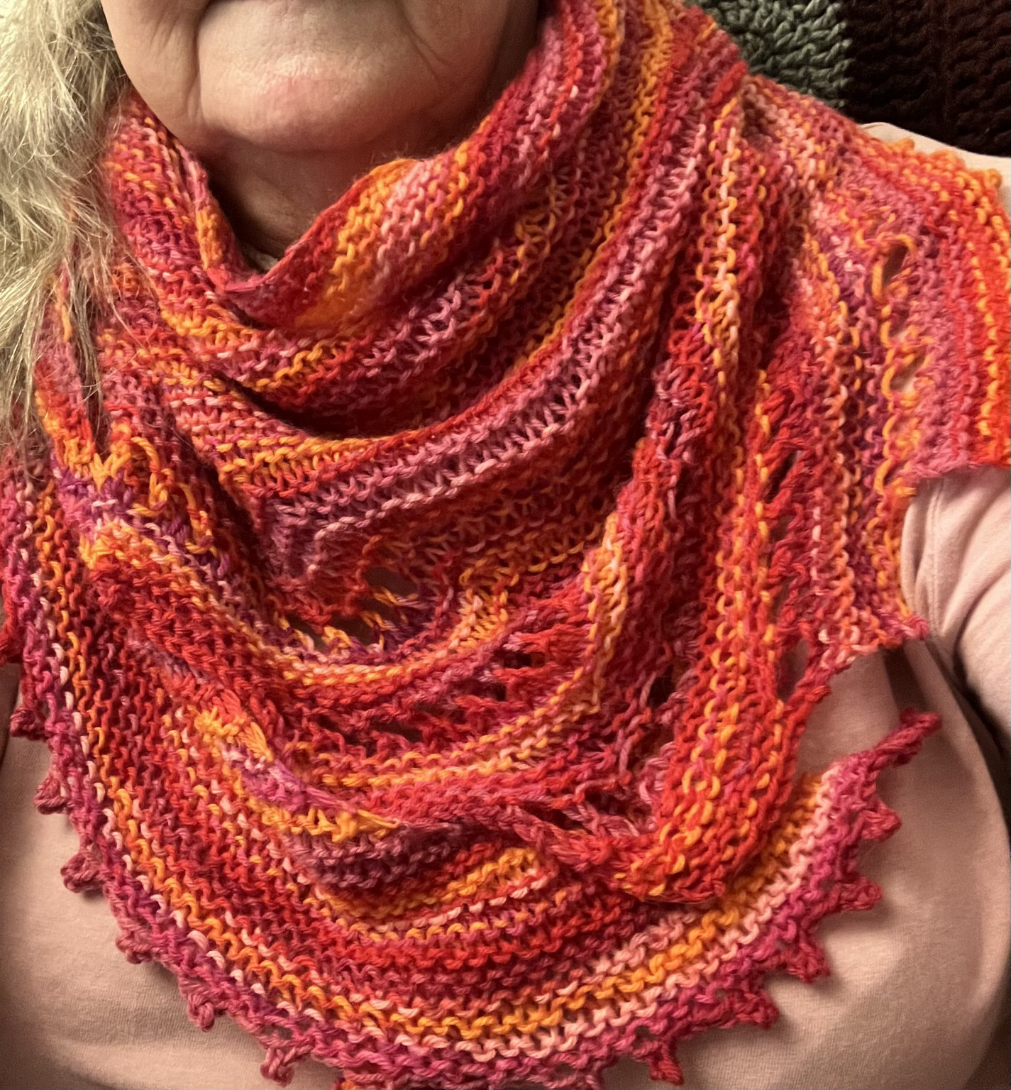 A knitted shawl in a variegated sock yarn of red, pink and orange.